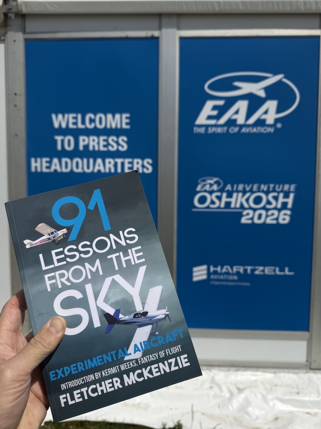 91 Lessons From The Sky — Experimental Aircraft, held up outside the EAA AirVenture Oshkosh 2026 press headquarters